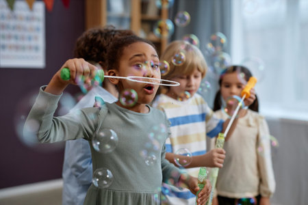 Group of joyful little kids playing with soap bubbles in preschool and laughing happilyの写真素材