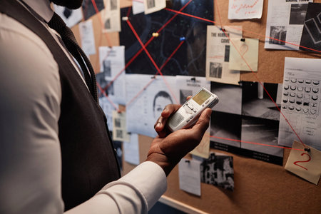 Close up of detective holding voice recorder while standing by evidence board, copy spaceの写真素材