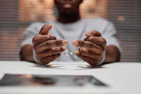 Close up of black man wearing handcuffs sitting at table in police department, copy spaceの写真素材
