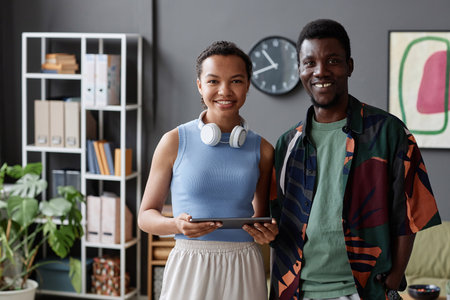 Waist up portrait of two young African American professionals smiling at camera standing in office,...
