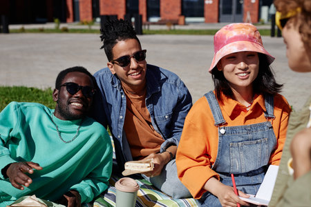 Vibrant portrait of diverse group of young students relaxing on grass outdoors and smiling happilyの写真素材