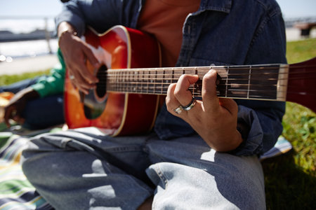 Close up of anonymous Black young man playing guitar outdoors with focus on male hands on strings
