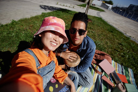 Colorful POV of diverse young couple taking selfie outdoors sitting on grass in sunlight, copy spaceの写真素材