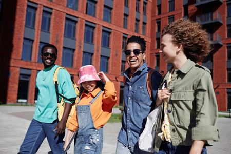 Group of young people walking together outdoors on modern college campus lit by sunlight