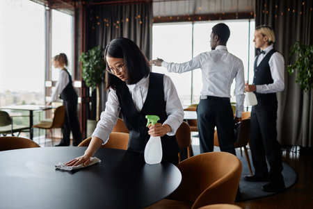 Luxury restaurant staff preparing for grand opening with focus on Asian young woman wiping dining...