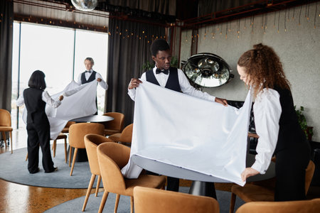 Group of elegant servers wearing classic uniforms preparing luxury restaurant for grand opening,...