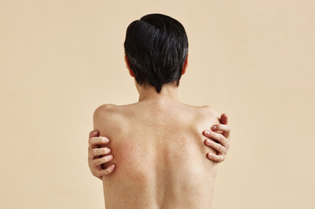 Minimal rear view of adult woman with bare back standing against beige background, copy space