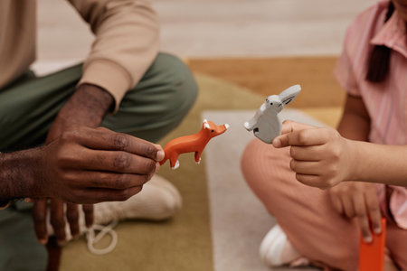 Close up of father and daughter playing with wooden toys and cute little animals, holding bunny and foxの写真素材