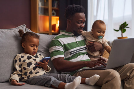 Portrait of young working father with two children using laptop and smiling enjoying parenting, copy...