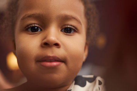 Close up portrait of cute Black little girl with big eyes looking at camera at home, bokeh effect, copy spaceの写真素材