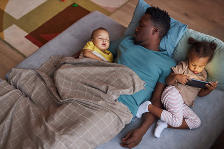 Top down view of exhausted Black father sleeping with two little kids at nap time