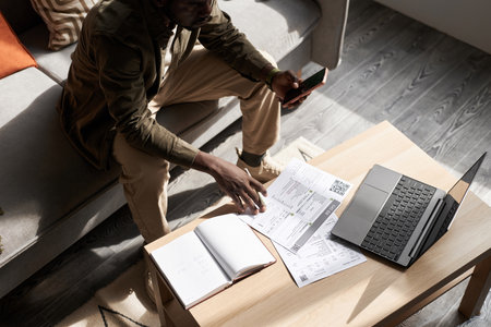 High angle portrait of Black adult man doing taxes at home in sunlight with financial documents on table, copy spaceの写真素材