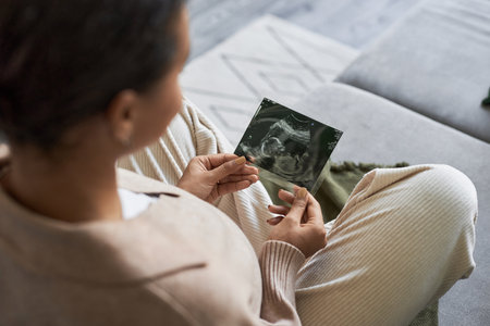 Portrait of pregnant young woman holding ultrasound picture of baby and enjoying motherhood, copy spaceの写真素材