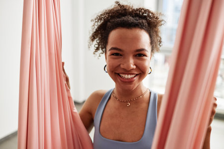Close up portrait of young Black woman smiling in pink hammock and enjoying aerial yoga in studioの写真素材
