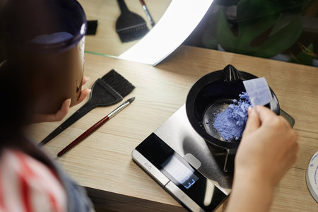 High angle closeup of hairstylist mixing bleach in plastic bowl and weighing solution on scales preparing to do hair coloring in beauty salon, copy spaceの写真素材