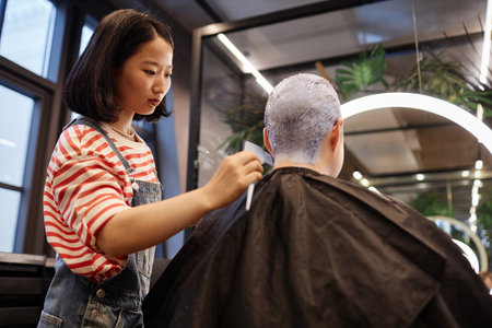 Waist up portrait of young Asian woman as hairstylist bleaching and dyeing hair of client in beauty salonの写真素材