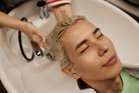 Top view closeup of young Asian man enjoying hair wash and haircare treatment in beauty salon sinkの写真素材