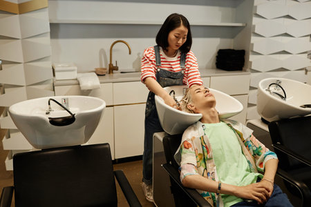 Portrait of young Asian man enjoying hair care treatment and wash in beauty salon sink, copy spaceの写真素材