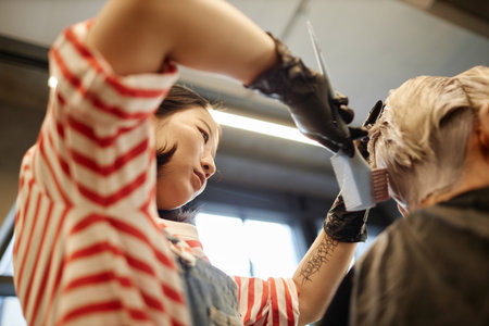 Low angle closeup of female hairstylist applying hair dye in modern beauty salonの写真素材
