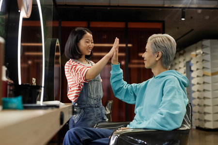 Side view portrait of young Asian man as client high five with hairdresser in beauty salonの写真素材