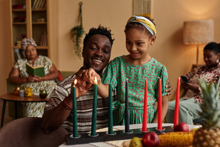 Father helping excited little daughter to light candles for Kwanzaa celebrationの写真素材