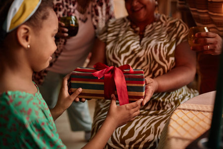 Grandmother giving Kwanzaa present to little girl when celebrating at home