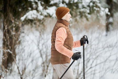 Senior woman in warm clothes skiing alone in forest on winterの写真素材