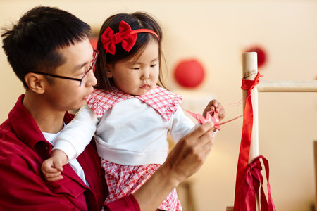 Side view portrait of caring Asian father with cute little girl decorating home for Chinese New Year...