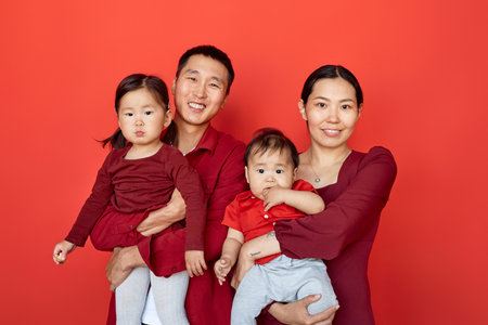Waist up portrait of happy Chinese family wearing red posing with two children on red background all smiling at cameraの写真素材