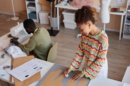 Young African American woman working with paper sewing patterns by workplace against her male...