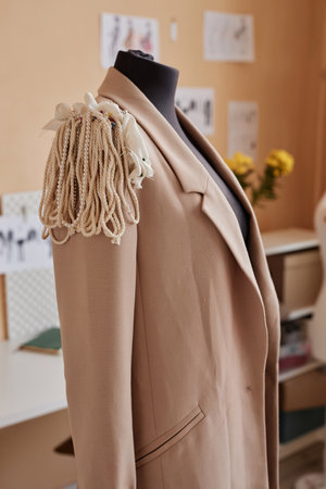 Blazer of beige color with handmade creative decoration on right shoulder hanging on dummy standing in front of camera in fashion studioの写真素材