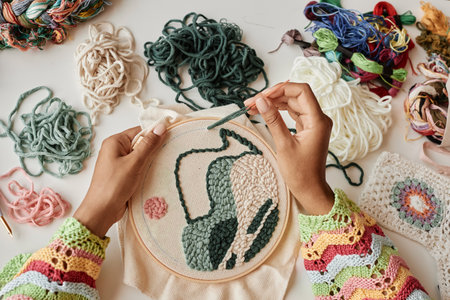 Above view of hands of young female designer making creative embroidery on piece of white canvas clamped in hoopの写真素材