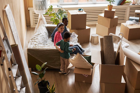 Long shot of young intercultural couple and their little son relaxing on couch covered with...