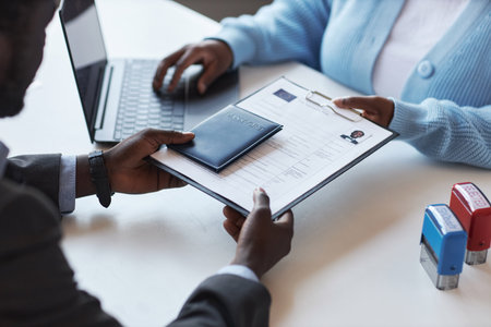 Hands of young African American male applicant passing documents and passport to female manager of...