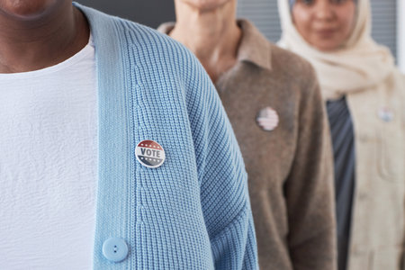 Close-up of young African American woman in blue cardigan with vote badge on chest standing in front of other voters during electionsの写真素材