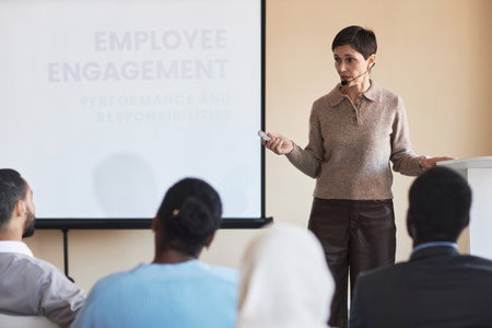 Confident mature female speaker standing by whiteboard during presentation of HR project to...