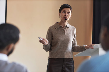Experienced HR manager speaking in microphone in front of audience while explaining them principles...