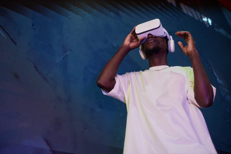 Futuristic low angle portrait of young Black man wearing VR headset against concrete wall, copy...