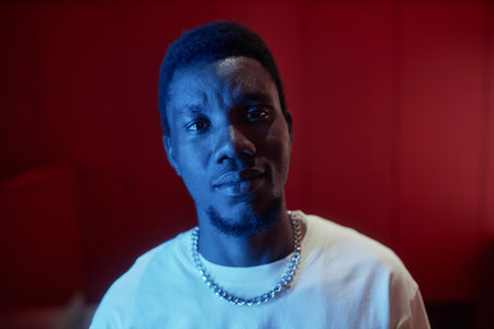 Futuristic portrait of young Black man looking at camera in contrasted neon light, copy space