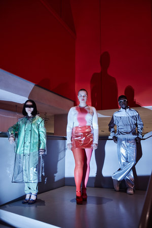 Group of three young people posing in futuristic outfits in neon lightsの写真素材