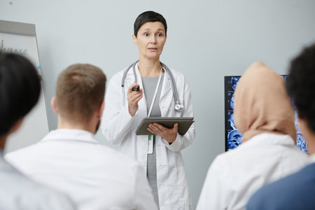 Waist up portrait of mature female doctor speaking to audience at medical seminar, copy spaceの写真素材