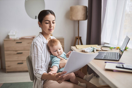 Portrait of young mother with baby working from home and reviewing documents, copy spaceの写真素材