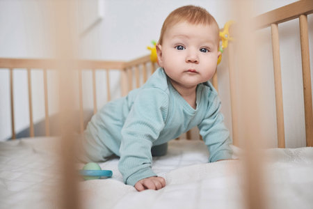 Close up of cute baby boy with blue eyes looking at camera while crawling in crib, copy spaceの写真素材