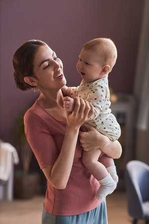 Candid portrait of young mother holding happy baby at home and smiling joyfullyの写真素材