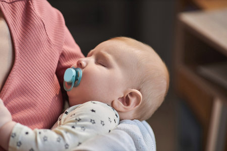Close up of cute sleeping baby with pacifier enjoying nap in mothers arms, copy space