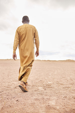 Back view of Black man wearing long caftan dress walking away from camera on sand dunesの写真素材