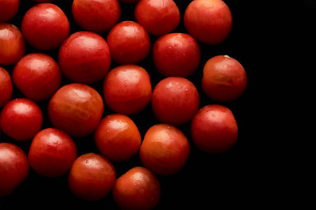 Top view closeup of ripe red cherry tomatoes laid out in abstract pattern on black background, copy spaceの写真素材