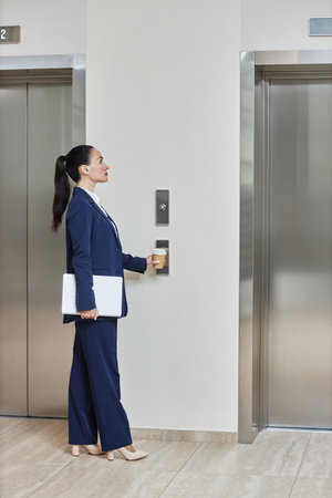 Full length shot of Caucasian brunette business lady wearing suit holding computer and paper cup...
