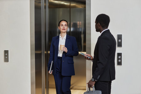 Medium long shot of diverse colleagues greeting each other by elevator. Smiling Caucasian business...