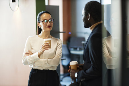 Medium shot of diverse colleagues chatting and standing in office building hall during coffee break,...
